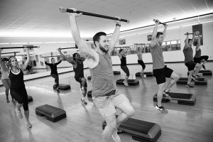 Photo of students lifting weights over their heads in a workout class