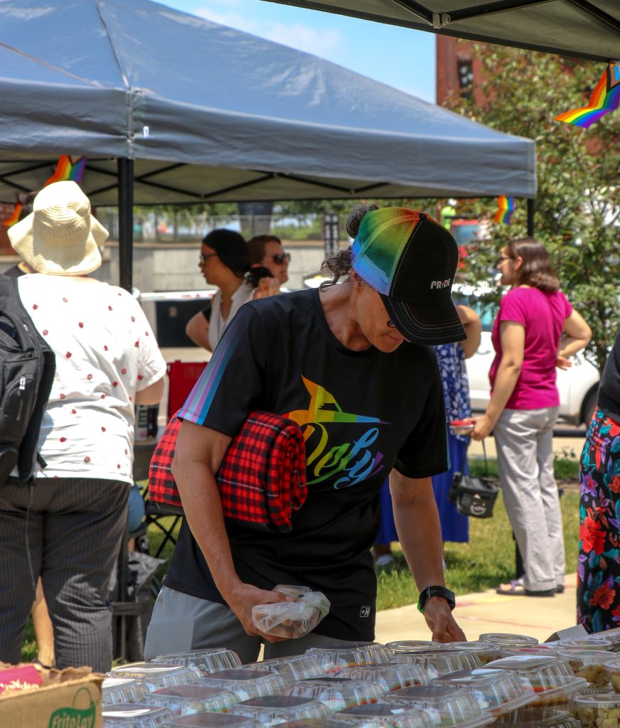 An attendee of the Pride Picnic grabs food under the tent at Library Mall. Attendee is wearing a rainbow hat and rainbow shirt.