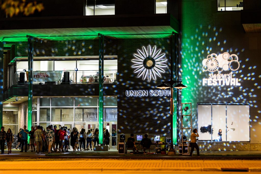 Spotlights shine on the exterior of Union South as people arrive for the Wisconsin Union Sunburst Festival at the University of Wisconsin-Madison at night.