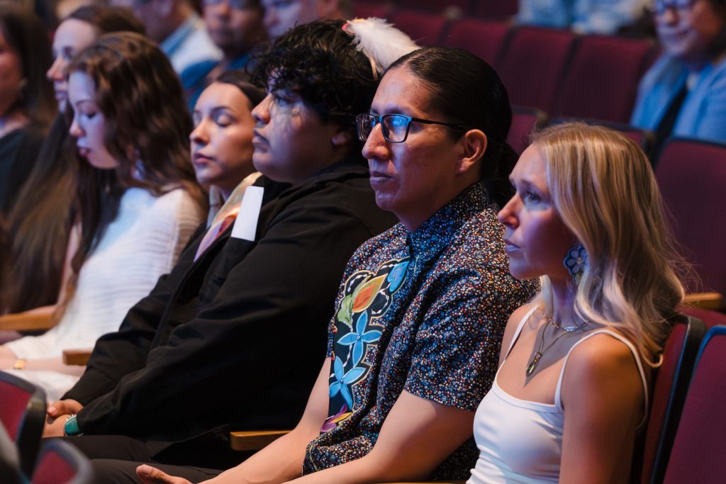 UW graduating seniors pictured from right to left are Keya Eden Allred, Karah LaTender, Miinan White, Eva Weddel, Kane Funmaker, and Miranda Jordan, listening to the speakers.