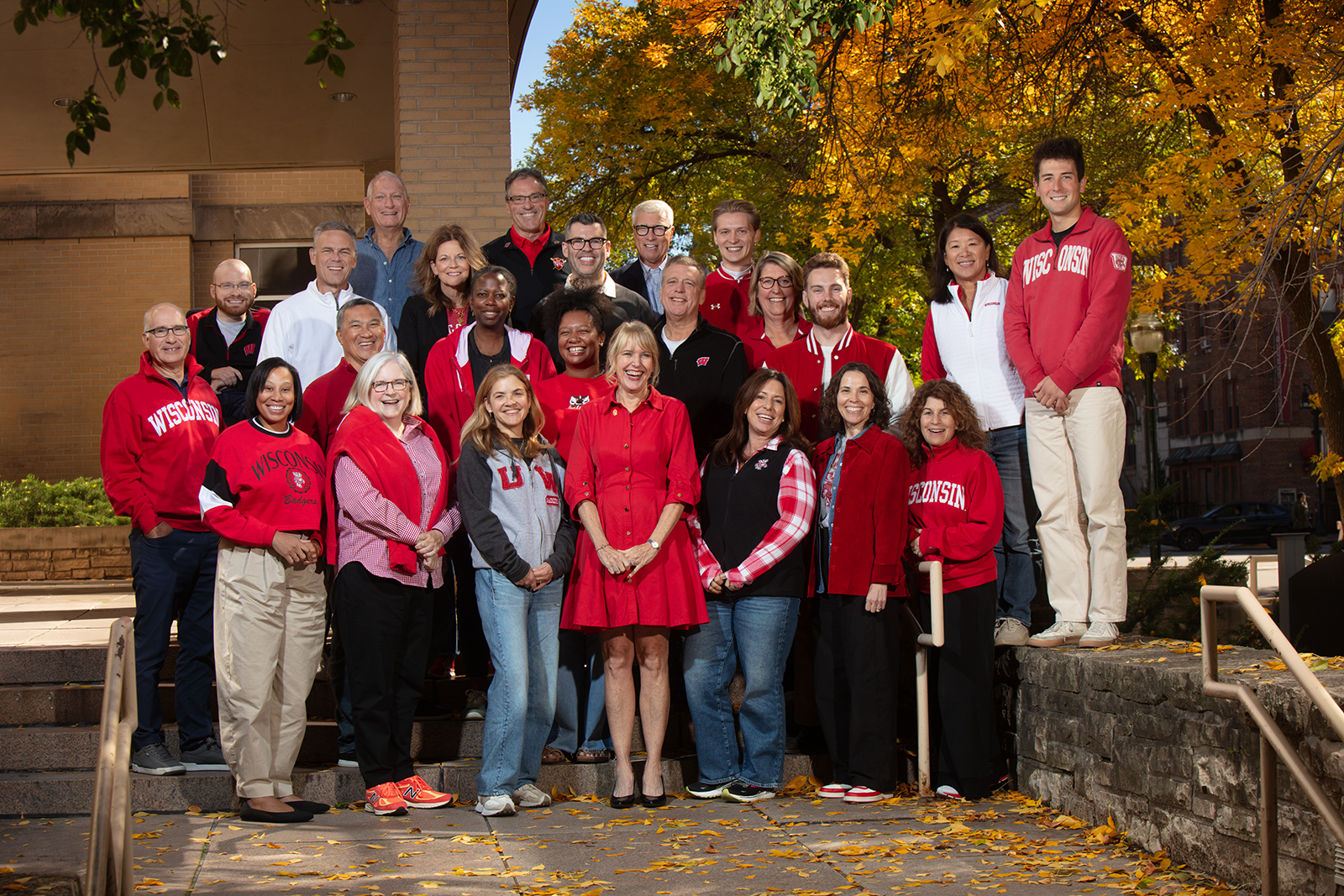 A photo of board members posing in front of a building and fall trees.