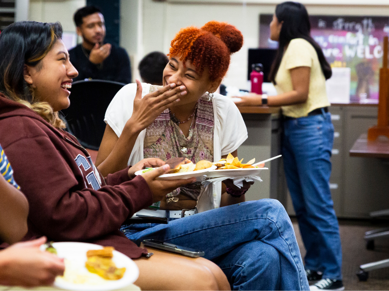 Two students share a laugh while eating at an event